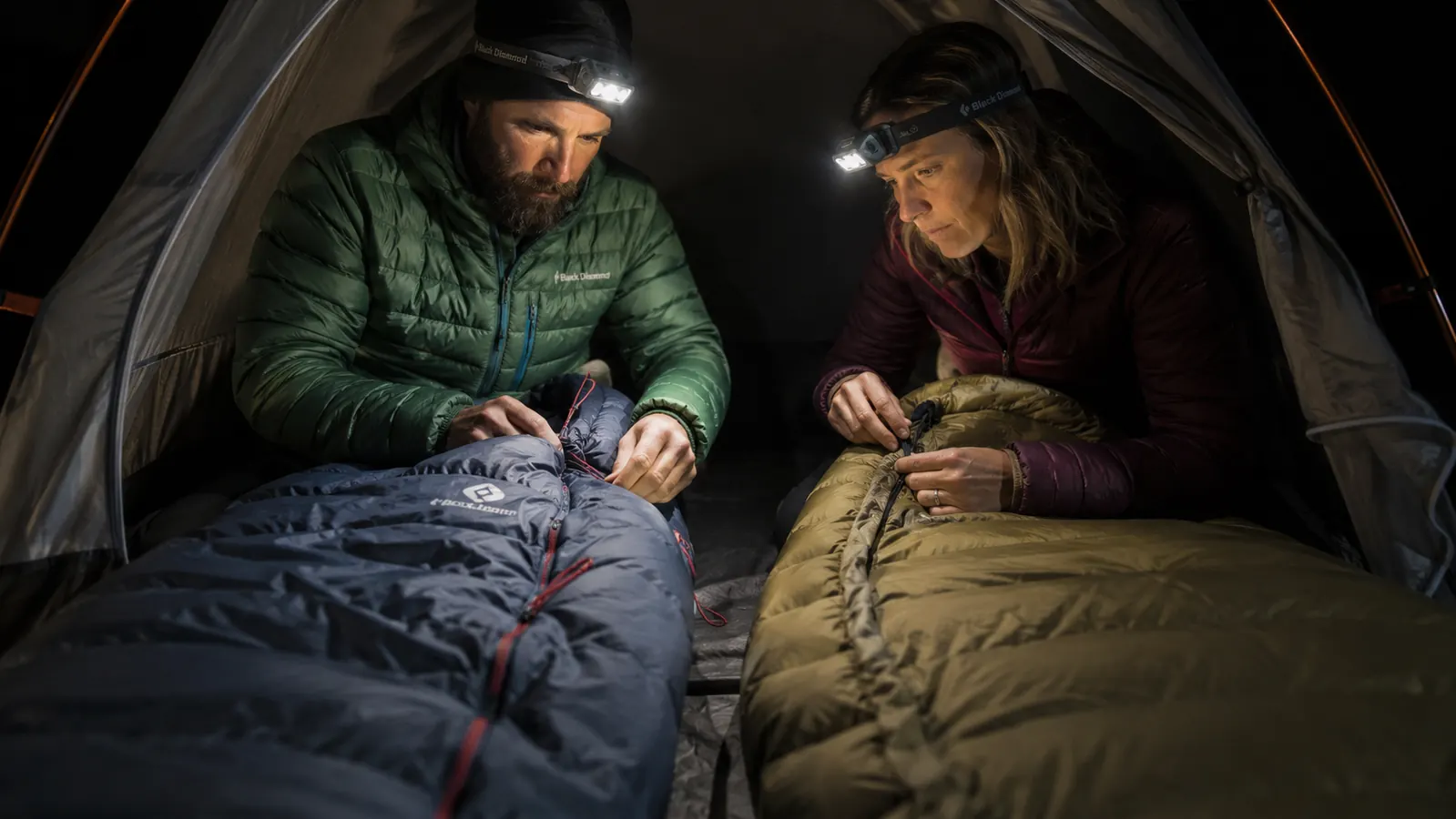Camper pulling a hood cinch cord tight on a mummy sleeping bag on a frosty morning at a backcountry campsite